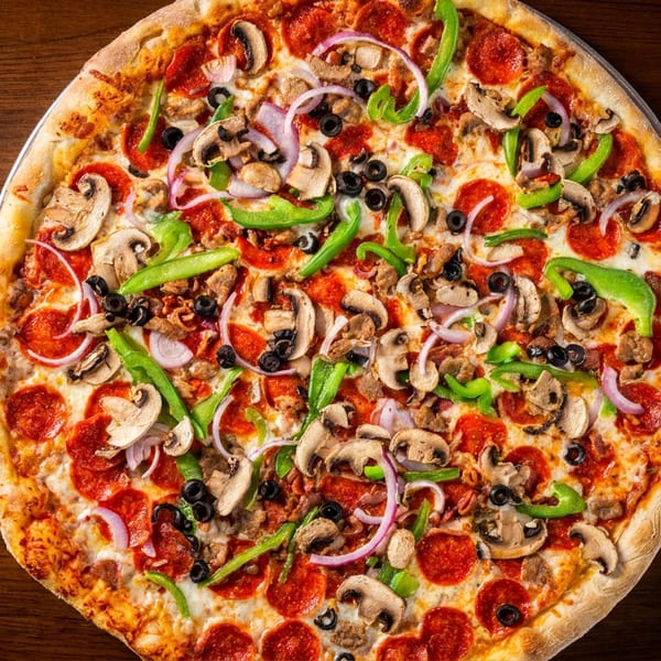 Delicious supreme pizza with pepperoni, mushrooms, green peppers, onions, and olives on wood.