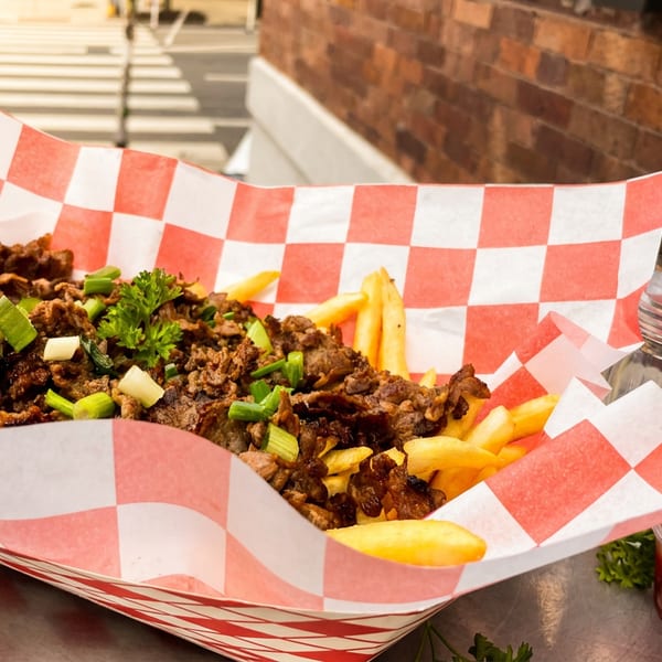 Loaded fries with seasoned meat, green onions, and parsley in a red and white checkered tray.