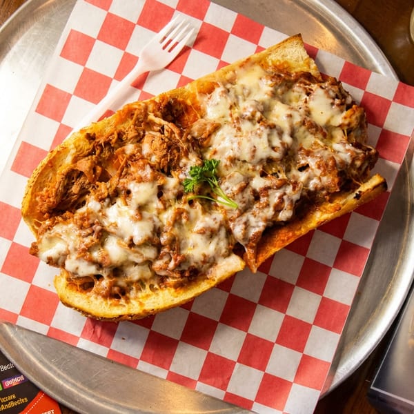 Large cheesy cheesesteak hoagie on a metal tray with checkered paper, next to a Carters menu.