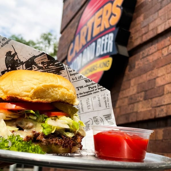 A delicious burger on a tray with ketchup, in front of a Carters Burgers and Beer sign.