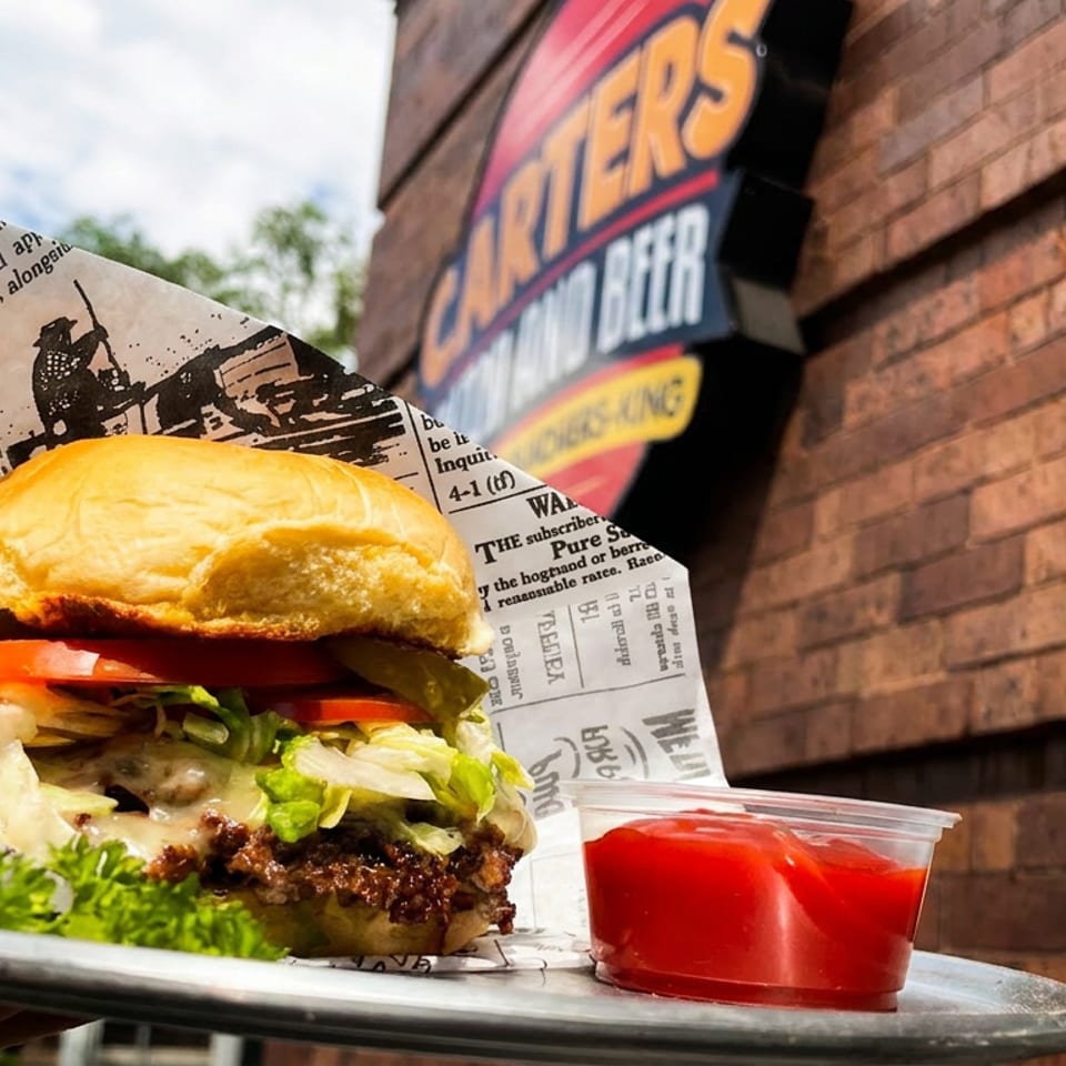 Cheeseburger with lettuce, tomato, and pickles on a tray with ketchup, outside Carter's Burgers and Beer.