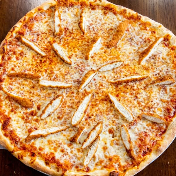 Whole pizza with melted cheese and chicken strips on a dark wooden table.
